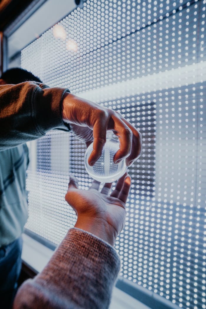 Close-up of hands holding a crystal ball in front of a vibrant LED wall display.