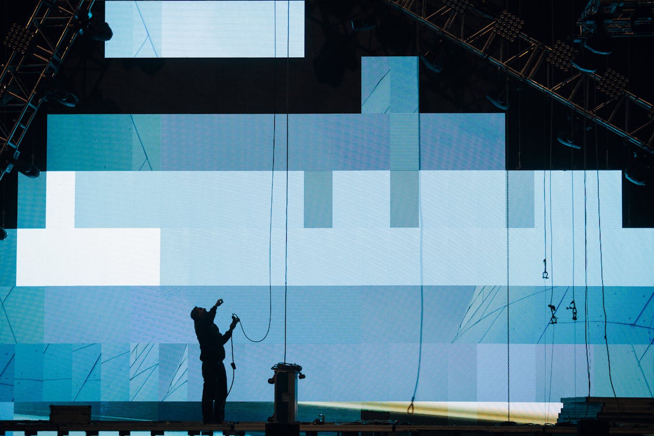 Side view of anonymous male worker silhouette setting up digital screen while looking up on stage